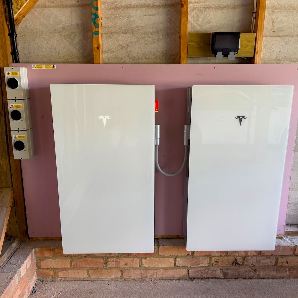 Two Tesla Powerwall 3 battery units installed side by side on a garage wall, connected via a harness for expanded storage capacity
