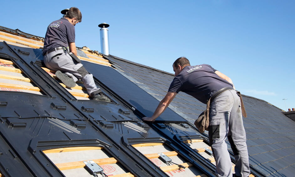 Two installers fitting solar panels to a pitched roof on a home in Windsor